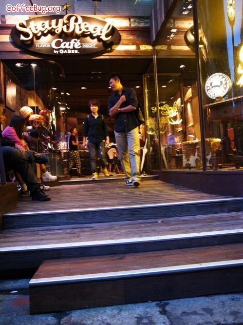 台北 StayReal Café——旅人归家
地址:台北敦化南路1段177巷21号
StayReal Café是阿信与不二良,继服饰店后,另一个跨足的品牌事业。爱喝咖啡,每天至少一、两杯纯美式咖啡的阿信和他的朋友们继续着年少时的梦想——开咖啡店。除非手上有正确的地址,若只是站在街头往巷内看,可能会错过它,唯有进入巷弄里,才会被它3米高的横式店招吸引,一旁还有难得的绿荫,底下的橱窗中,展现着老板阿信与他高中好友不二良对“家”的坚持。
StayReal Café是一家营造旅人回家感觉的咖啡馆。进入店内,就能感受到这里艺术味浓厚的氛围,右面墙上,挂着多幅村上龙与香港艺术家Molly by Kenny的作品,左边陈列着“一克拉的梦想”艺术展周边商品,让展出时没到的人,可在这里挑选。连菜单也编排得像一本精美图文书,从试营运到正式开店,它已被翻得快变形了。让员工们感动的是,店里的所有陈设,举凡画作、皮制复古沙发、木箱或皮箱,到最里面的个人珍藏柜里的宝物,甚至只是灯光角度,阿信都会自己动手调整。也就是说,也许你坐的位子,可能是大明星前一晚来时调整过的!